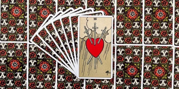 A imagem na carta mostra um coração perfurado por três espadas, flutuando sob um céu pesado e nublado, com chuva caindo ao fundo.