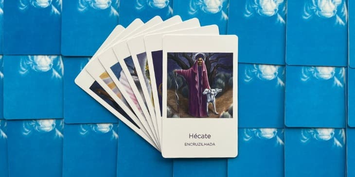 a deusa hecate com um manto roxo, um cachorro branco de 3 cabe�as e um bast�o em formato de cobra na outra m�o.