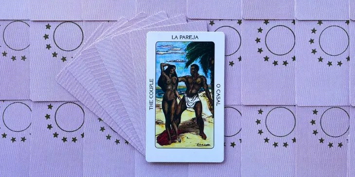 um casal de homem e mulher negros, est�o nus em uma praia com um coqueiro ao fundo, o mar e um lindo ceu azul.
