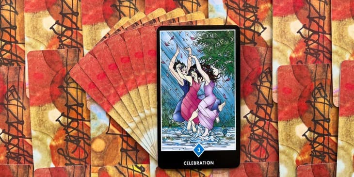 carta do tarot zen osho onde mostra 3 mulheres dan�ando na chuva, cada uma com um vestido de cor diferente e felizes dan�ando na chuva.
