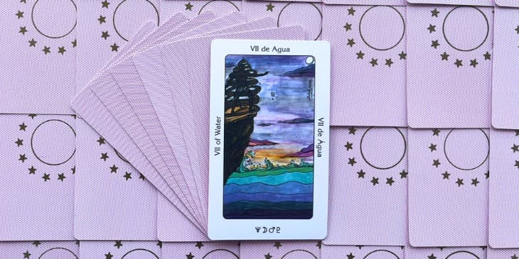 uma carta do tarot dos orixas em cima de uma mesa com varias outras cartas rosas espalhadas pela mesa