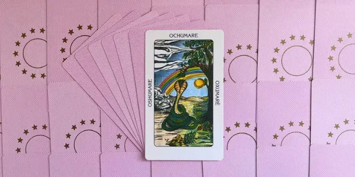 uma cobra ou serpente verde ao lado de uma arvore com um arco-iris no ceu azul.
