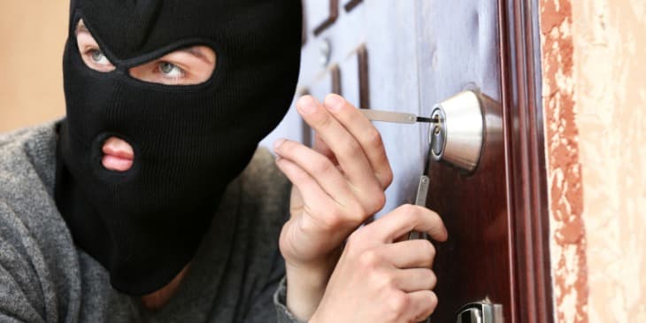 um homem branco de mascara abrindo uma porta para roubar uma casa