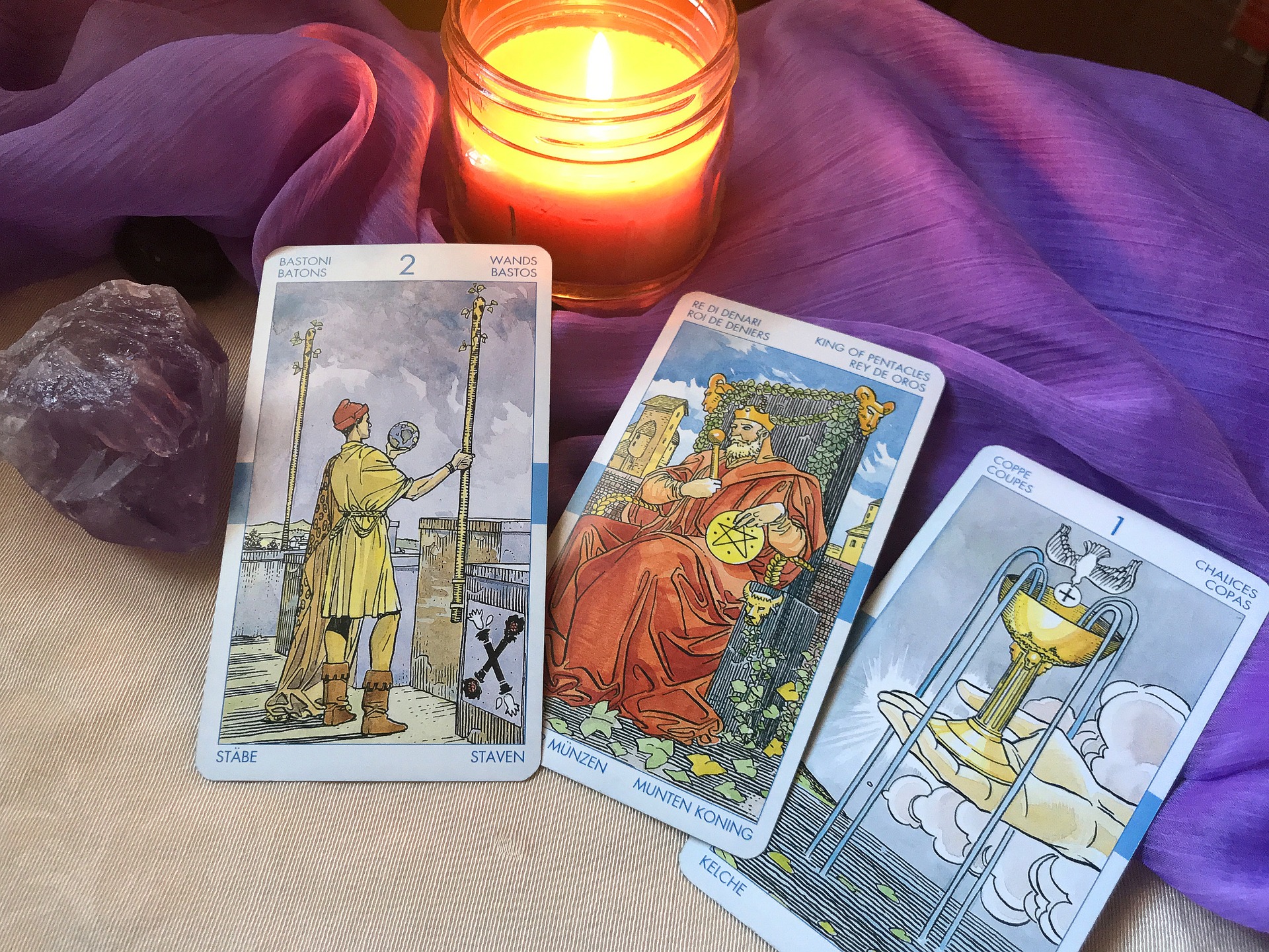 3 cartas de tarot em cima de um pano roxo e uma vela