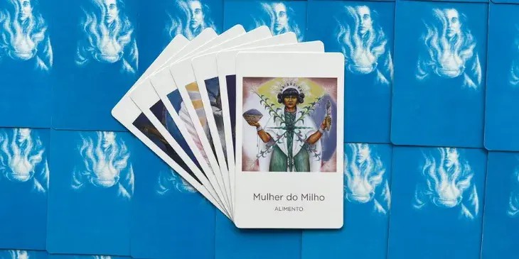 a deusa mulher do milho segurando um alguidar em uma mao e uma raiz na outra com um cocar