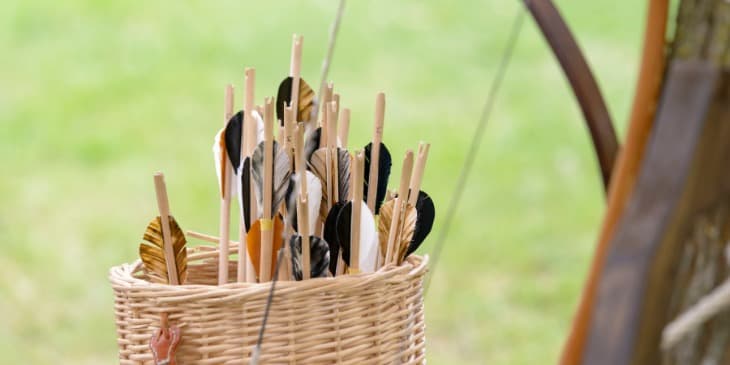 varias flechas de madeira com penas na ponta em um cesto de palha