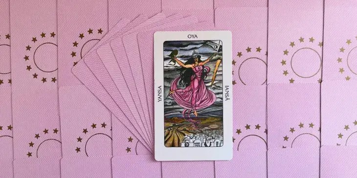 Orixa Ians� ou Oi� vindo das nuvens cheias de raios com seus bra�os para cima, um dos bra�os tem nove pulseiras do mesmo material que a coroa, no outro bra�o uma das ferramentas que usa, usa um vestido comprido rosa, uma coroa na cabe�a e um lindo cabelo preto comprido.