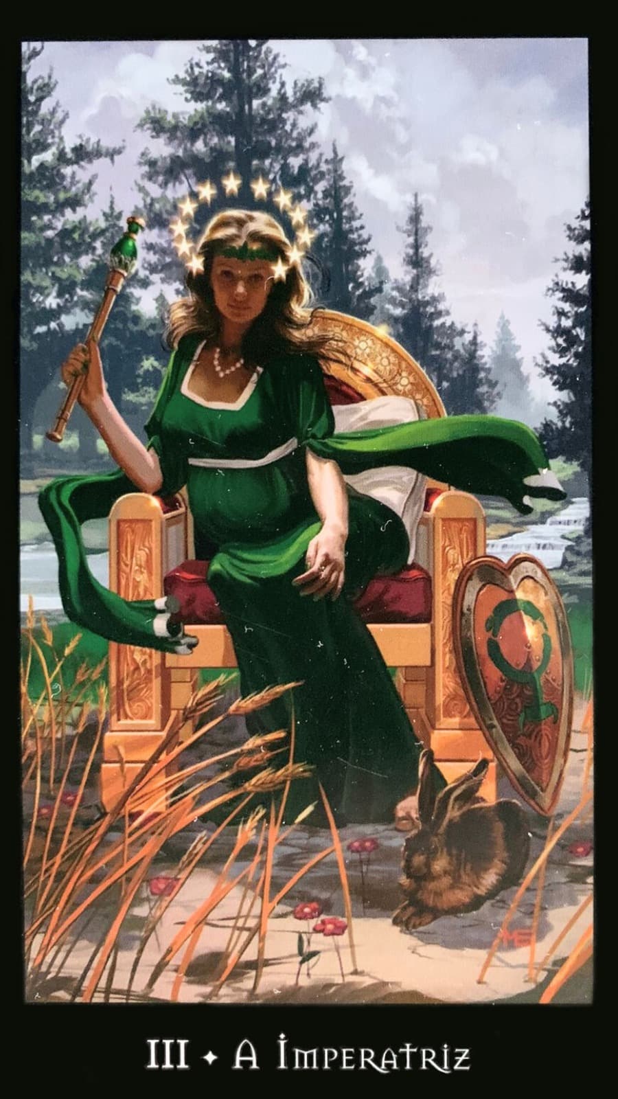 carta do tarot das bruxas a imperatriz onde mostrar a figura de uma mulher sentada em um trono de vestido verde e uma coroa, ao lado do trono tem um escudo e um coelho ao ar livre