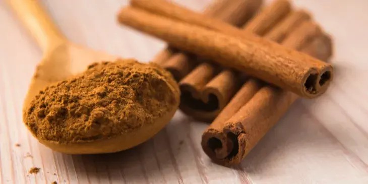 uma colher de pau cheia de p� de canela e canela em pau