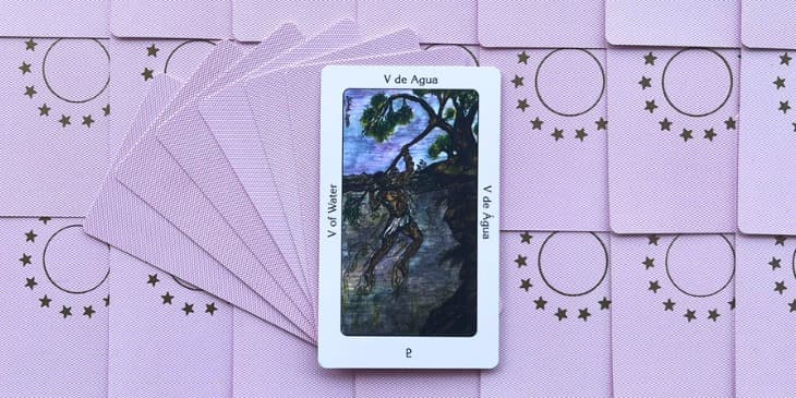 uma carta do taro dos orixas o cinco de agua em uma mesa com varias outras cartas