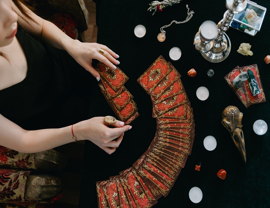 uma mesa com varios oraculos na mesa e uma tarologa tirando as cartas de tarot