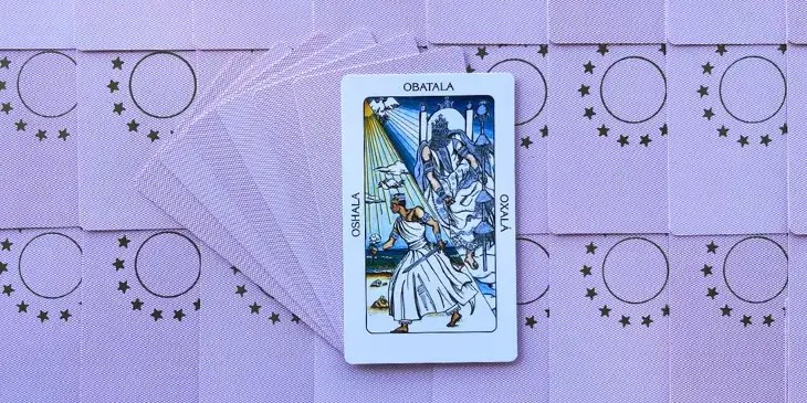 na parte de baixo da carta um jovem oxala como um guerreiro segurando uma espada em uma mao e uma rosa branca em outra com uma coroa azul e um passaro branco voando sobre sua cabe�a, na parte de cima da carta vemos oxala mais velho sentado em um trono branco com seu vestido branco e uma pomba branca no ceu.
