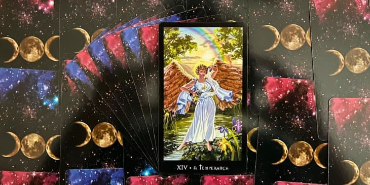 Carta do Tarot das bruxas que mostra uma mulher com um par de asas douradas e uma tunica branca, ela esta ao lado de um lago com os pes descal�os e no fundo tem um arco iris e um sol.